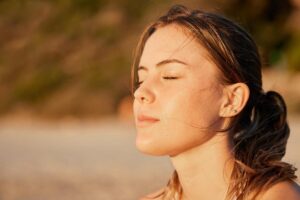 a woman sits on a beach with her eyes closed facing the setting sun while understanding the importance of diagnosing co-occurring disorders