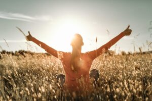 a person in a farm field has hands raised after achieving many of their addiction recovery goals