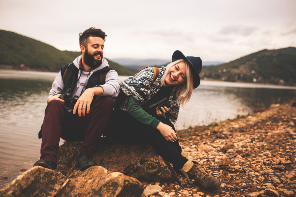 man and woman laughing and sitting on rock with lake in background