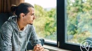 man looking out window with sad look