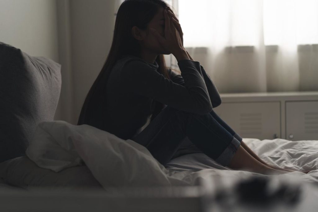 woman in bed with head in hands considering preventing addiction relapse