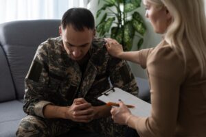 an adult man sits hunched over in distress while talking to therapist about substance abuse in the military