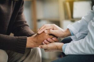 two people sit with one person holding another person's hands to comfort them while explaining how an outpatient treatment program can help 